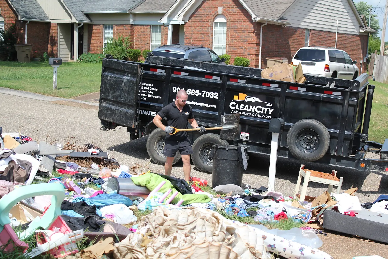 A crew member shoveling a curbside pile into a Clean City dump trailer