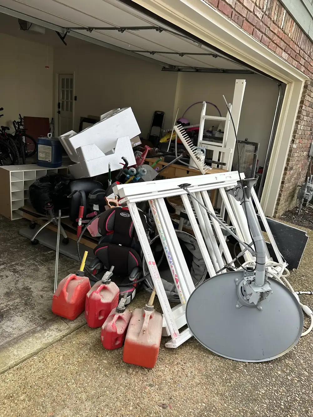 A garage full of furniture, gas cans and a satellite dish before a cleanout