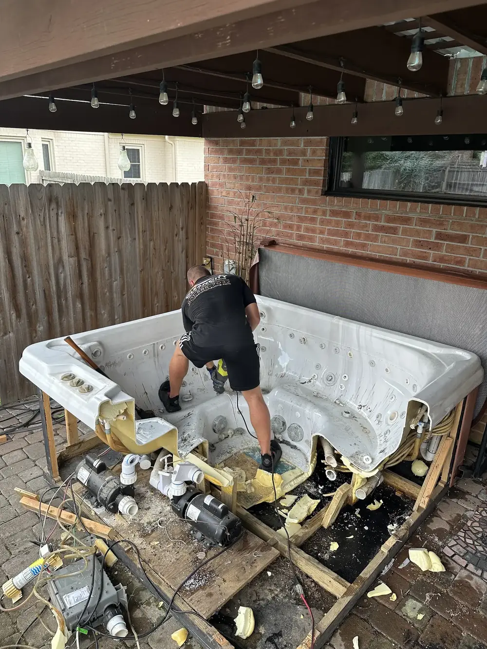 A crew member cutting apart a hot tub on a patio